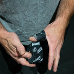 Person holding a roll of black tape with white text, wearing a gray shirt.