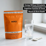 Orange package of HIRO Clean Creatine with a glass of water and scoop on a light surface.