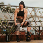 Woman exercising outdoors with a kettlebell on a metal bridge.