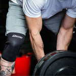 Person lifting weights with a knee brace on, focusing on the action and equipment used.